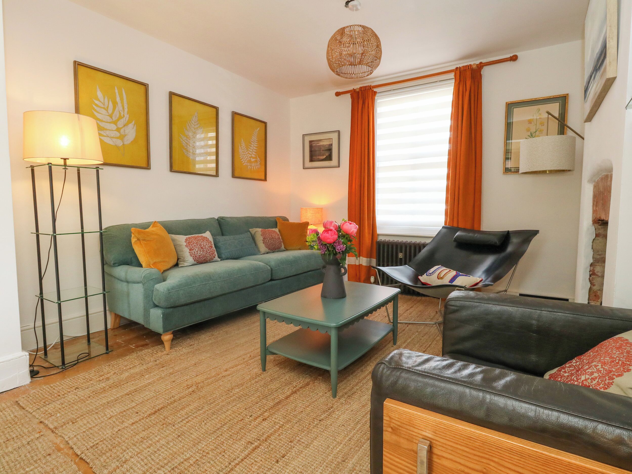 A living room with a sofa, a coffee table, a chair, a floor lamp, and a vase with flowers.