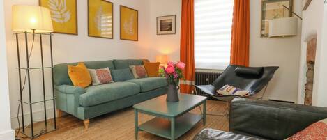 A living room with a sofa, a coffee table, a chair, a floor lamp, and a vase with flowers.