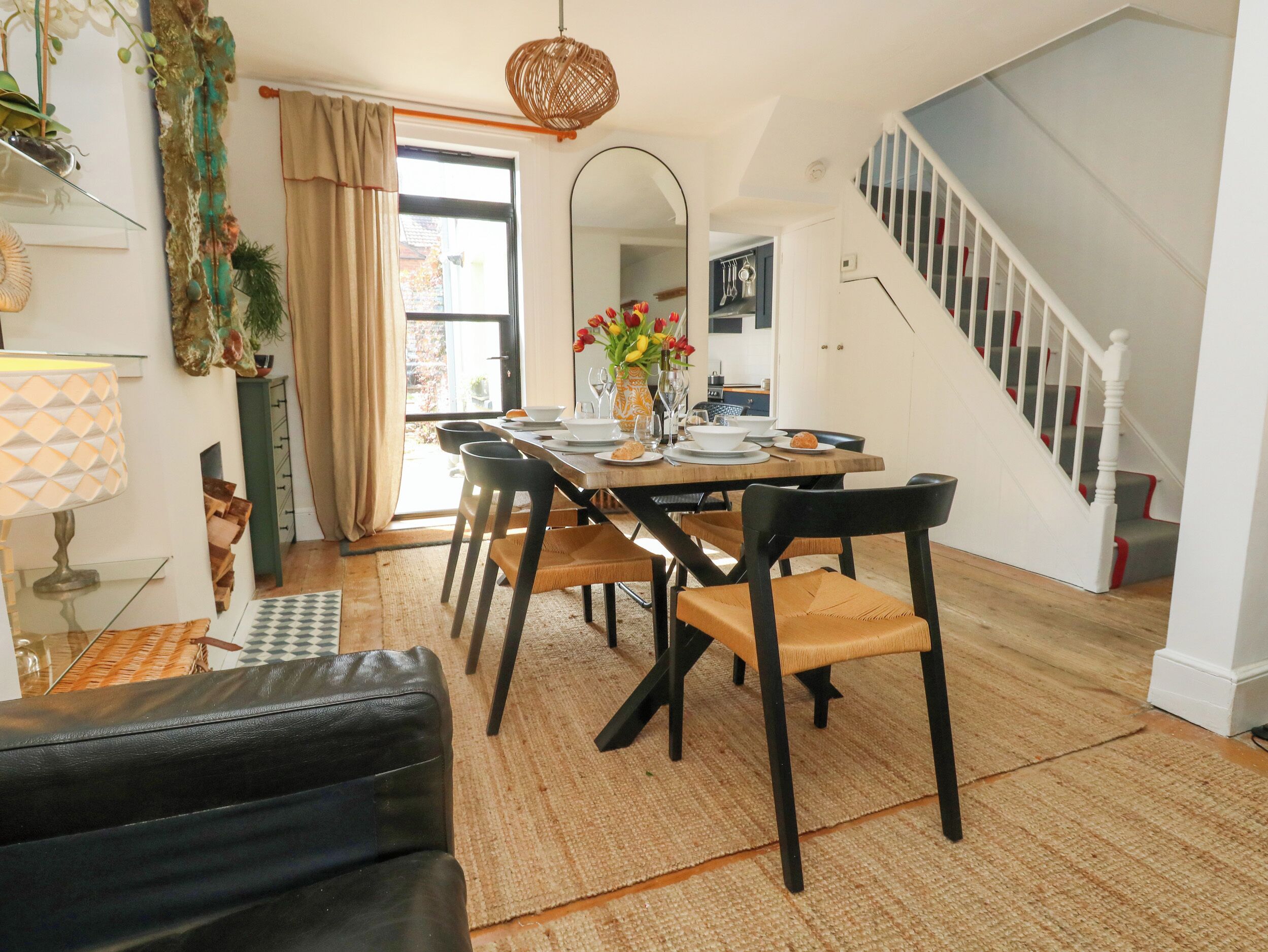 A dining area with a wooden table, black chairs, and a vase of flowers. A staircase leads to another room.