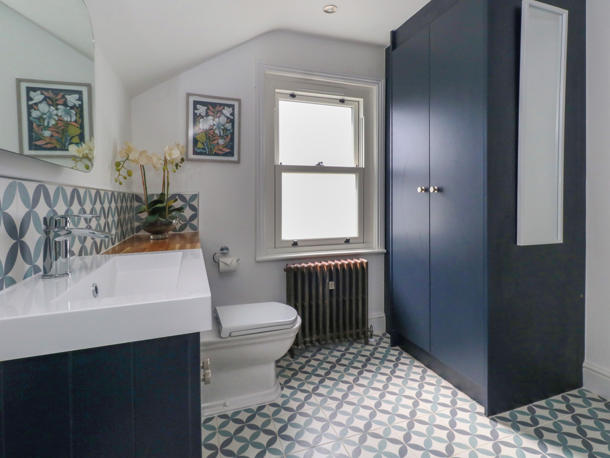 A bathroom with a white toilet, a sink with a mirror, a window, and a radiator.