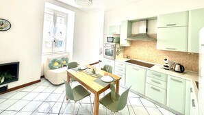 A compact kitchen with a dining area, featuring a wooden table, green chairs, and basic appliances. - Over the Rainbow in Sant Agnello (Sant'Agnello)