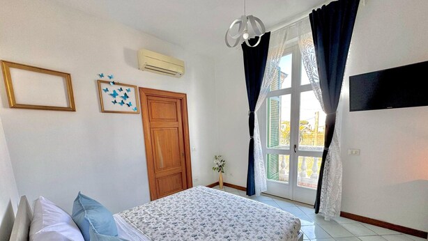 A bedroom with a bed, a wooden door, an air conditioner, and a window with curtains. - Over the Rainbow in Sant Agnello (Sant'Agnello)