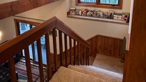 A wooden staircase with a handrail leading to a landing with a window overlooking a forest.