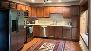 A kitchen with wooden cabinets, stainless steel appliances, a chandelier, and a patterned rug.
