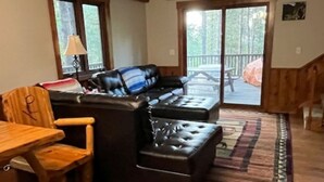 A cozy living room with a wooden ceiling, a leather sofa, a wooden dining table, and a stone fireplace.