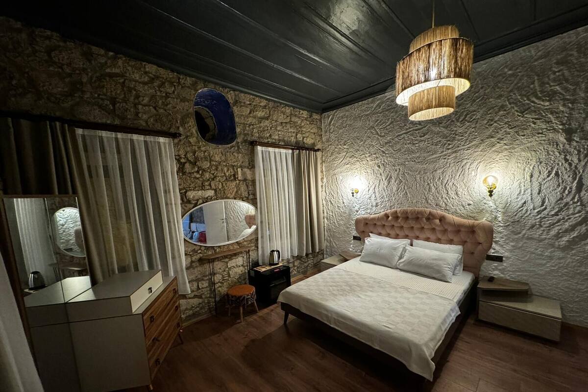 A bedroom with a stone wall, a wooden bed, a dresser, a mirror, and a hanging light fixture.