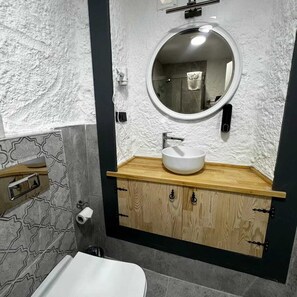 A bathroom with a round mirror, wooden vanity, and a toilet. - Baba Evi Alaçatı (Cesme)