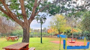 A park with picnic tables, a swing set, and a playground. - Spacious, Peaceful 2BD, Mamad, Garden, Parking near Kfar Sava (Gan Haim)