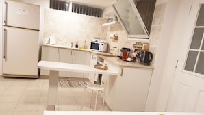 A compact kitchen with white cabinets, a microwave, and a small dining table. - Spacious, Peaceful 2BD, Mamad, Garden, Parking near Kfar Sava (Gan Haim)