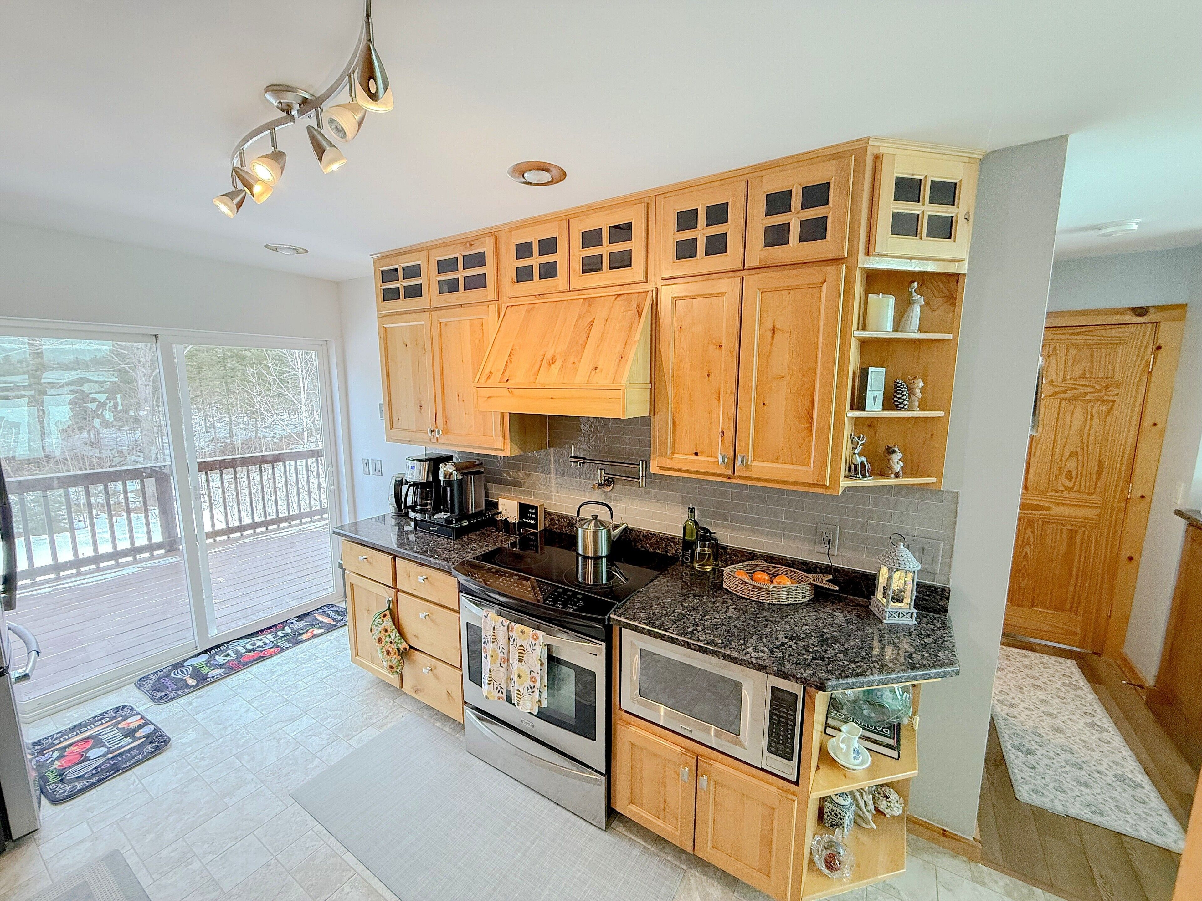 A modern kitchen with wooden cabinets, granite countertops, stainless steel appliances, and a large window.