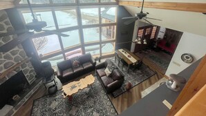 A high-ceilinged living room with a fireplace, a large window, and a ceiling fan. - Peaceful Getaway on Mio Pond (Mio)