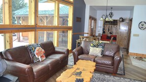 A living room with two brown leather sofas, a wooden coffee table, and large windows overlooking a wooden deck. - Peaceful Getaway on Mio Pond (Mio)