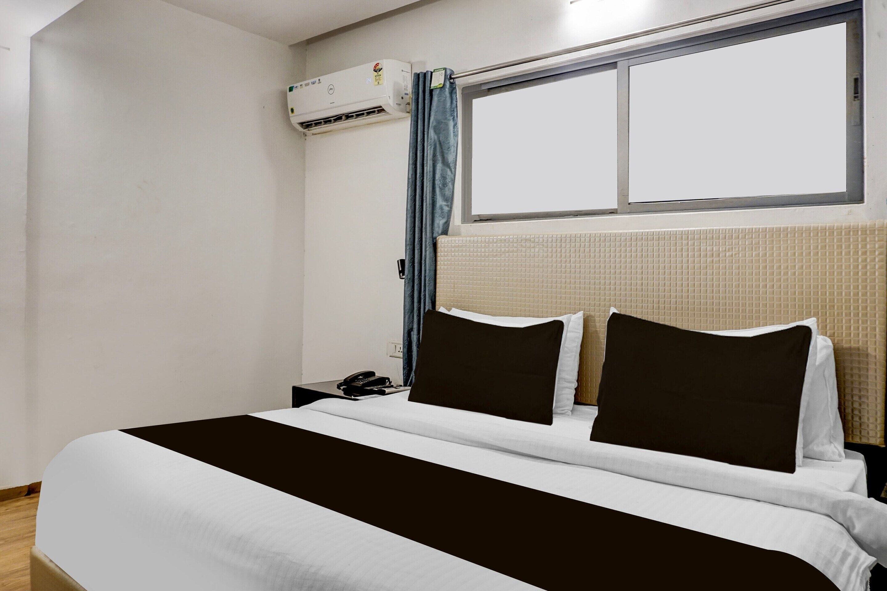 A hotel room with a bed, a nightstand, a telephone, and a window with curtains.