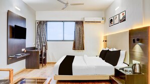 Habitación de hotel moderna con cama, escritorio, silla, televisor, ventilador de techo y ventana con cortinas.