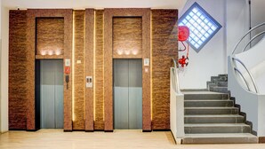 Un ascensor moderno con revestimiento similar a madera, un teléfono rojo de emergencia y una ventana con diseño de cuadrícula.