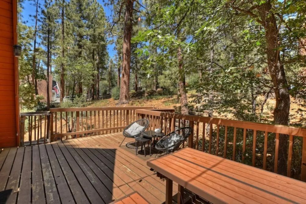 A wooden deck with a table and chairs, surrounded by tall trees.