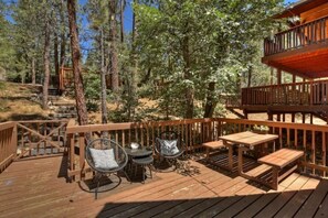 A wooden deck with outdoor furniture, surrounded by trees. - Acute A-frame Cabin w/ WiFi, close drive to lake! (Big Bear)