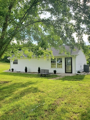 A single-story house with a front porch, a small garden, and a tree providing shade.
