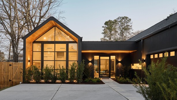 Una casa moderna con un'ampia vetrata, un patio in legno e un giardino curato.