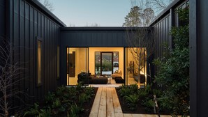 Una casa moderna con una terrazza in legno che conduce a un soggiorno con vetrate e dotato di divano e tavolo.