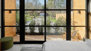 Una camera da letto con una grande finestra, un letto, un poggiapiedi verde e vista sull'esterno.