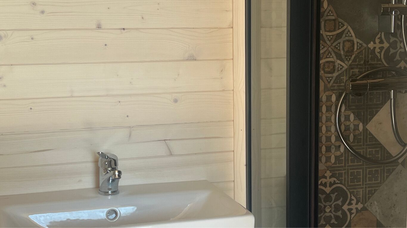 A bathroom with a wooden panel wall, a white sink with a chrome faucet, and a shower area with patterned tiles.
