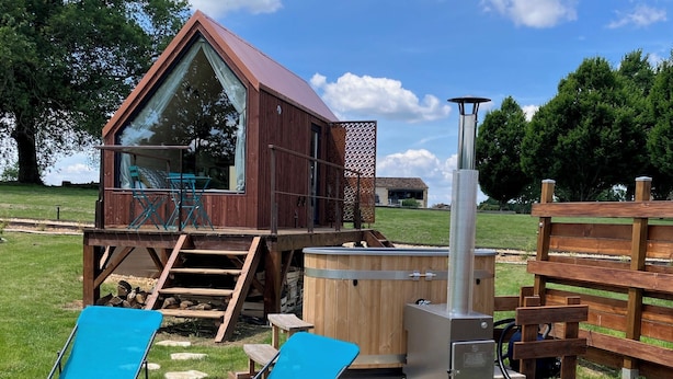 Une cabane en bois avec une fenêtre en verre, un jacuzzi et deux chaises bleues.