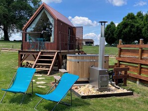 Une cabane en bois avec une fenêtre en verre, un jacuzzi et deux chaises bleues.