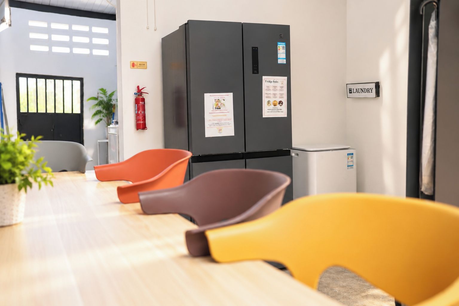 A modern kitchen with a black refrigerator, a small trash bin, and a sign indicating a laundry area.