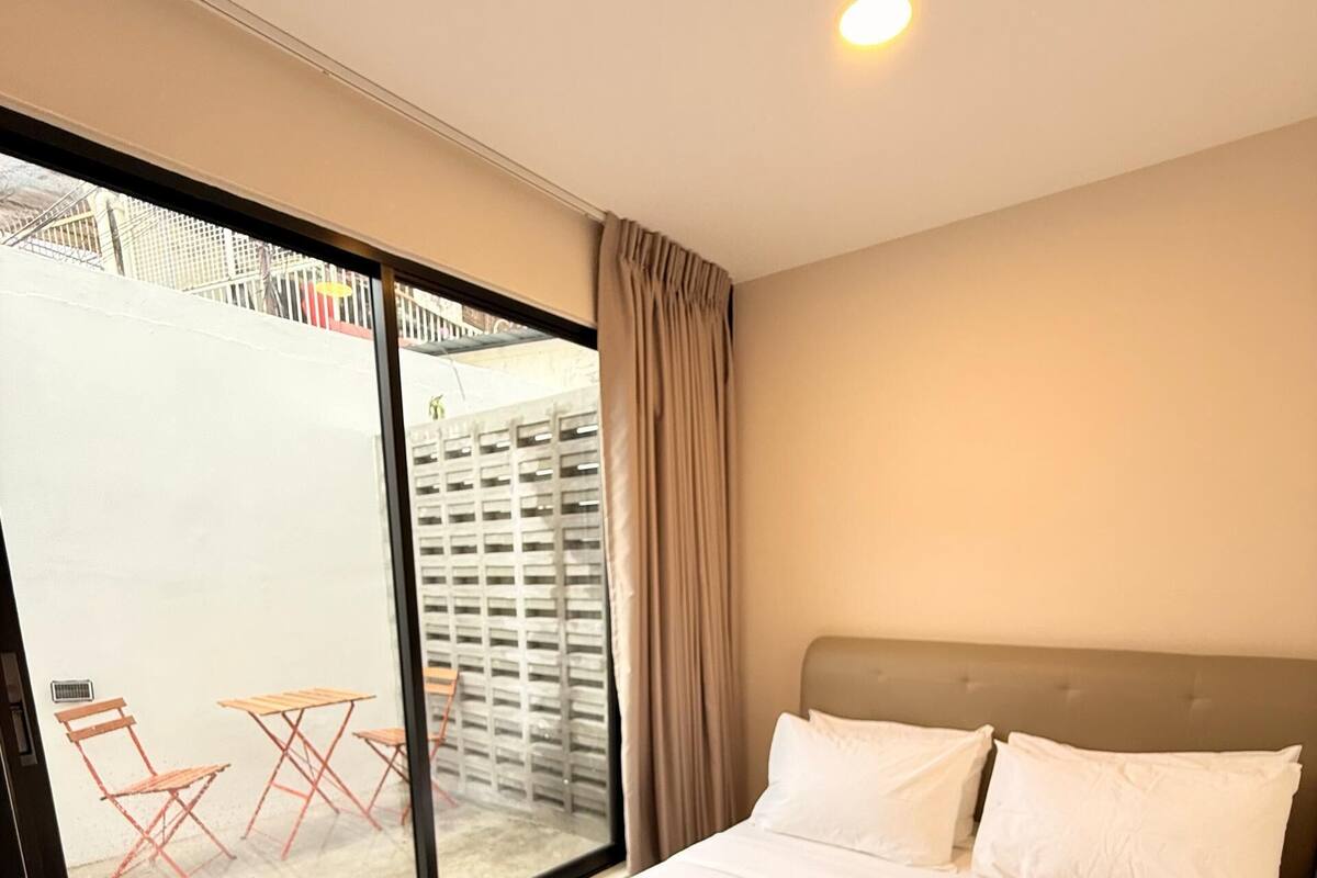 A hotel room with a large bed, a window with a view of outdoor seating, and a ceiling light.