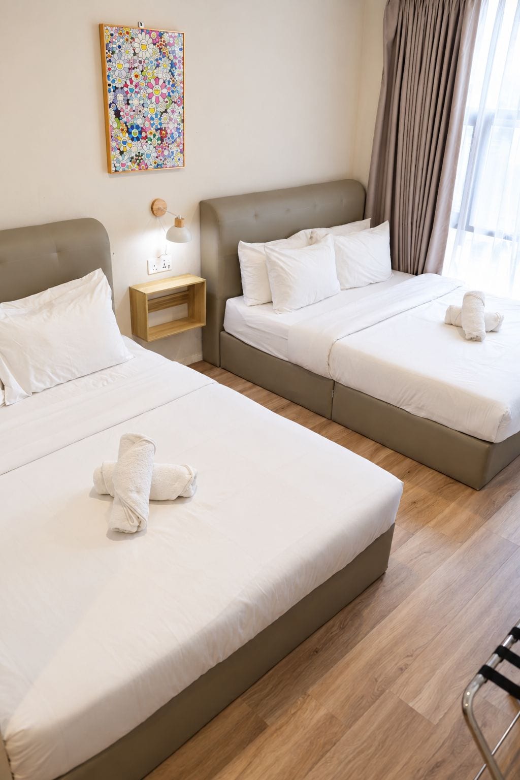A hotel room with two beds, a bedside table, a lamp, and a colorful artwork on the wall.