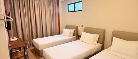 A hotel room with two single beds, a small table with a chair, and a window with curtains.