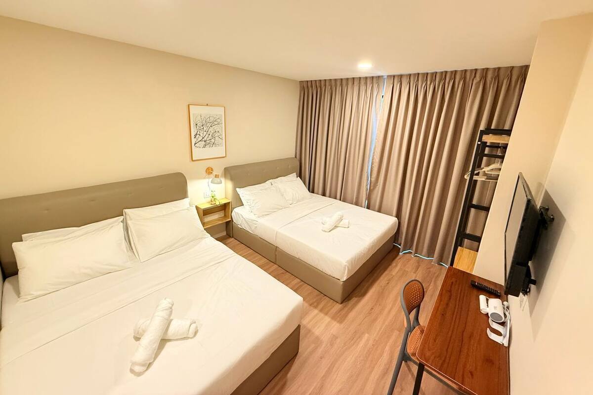 A hotel room with two beds, a desk, a chair, a TV, and a window with curtains.