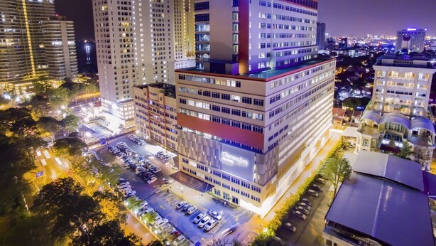 A multi-story hotel with a prominent sign, surrounded by other buildings and a parking lot. - TwinTrees Kelawai (George Town)