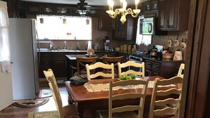 A kitchen with dark wooden cabinets, a dining table with chairs, a chandelier, and a refrigerator. - Charming 4-bedroom farmhouse in delightful Hinton with WiFi, AC (Hinton)