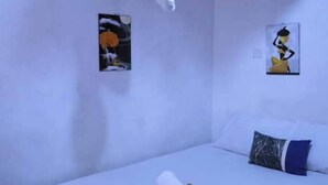 A bedroom with a bed, a pillow, a rolled towel, and two wall art pieces. - Lux Suites Ruby Court Apartments Kisumu (Kisumu)