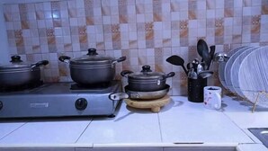 A kitchen with a gas stove, pots, a coffee maker, and a fan. - Lux Suites Ruby Court Apartments Kisumu (Kisumu)