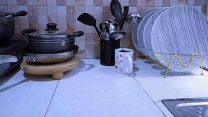 A kitchen with a tiled backsplash, a wooden cutting board, a pot on a stove, a coffee mug, and a metal strainer. - Lux Suites Ruby Court Apartments Kisumu (Kisumu)