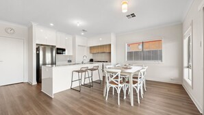 A modern kitchen with white cabinetry, a stainless steel refrigerator, and a dining area with white chairs and a wooden table. - 29 Blanche Pd, Hindmarsh Island (Hindmarsh Island)