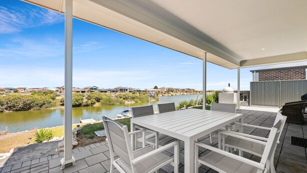 An outdoor patio with a table and chairs, overlooking a body of water and a residential area. - 29 Blanche Pd, Hindmarsh Island (Hindmarsh Island)