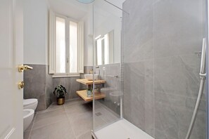 A modern bathroom with a glass-enclosed shower, a toilet, a sink with a wooden countertop, and a potted plant.