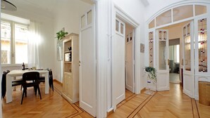 Een ruime kamer met een houten vloer, witte muren en een eethoek met een tafel en stoelen.