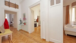 Een ruime woonkamer met een houten visgraatvloer, een bank, een zitbankje en een rode jas hangend aan een deur.