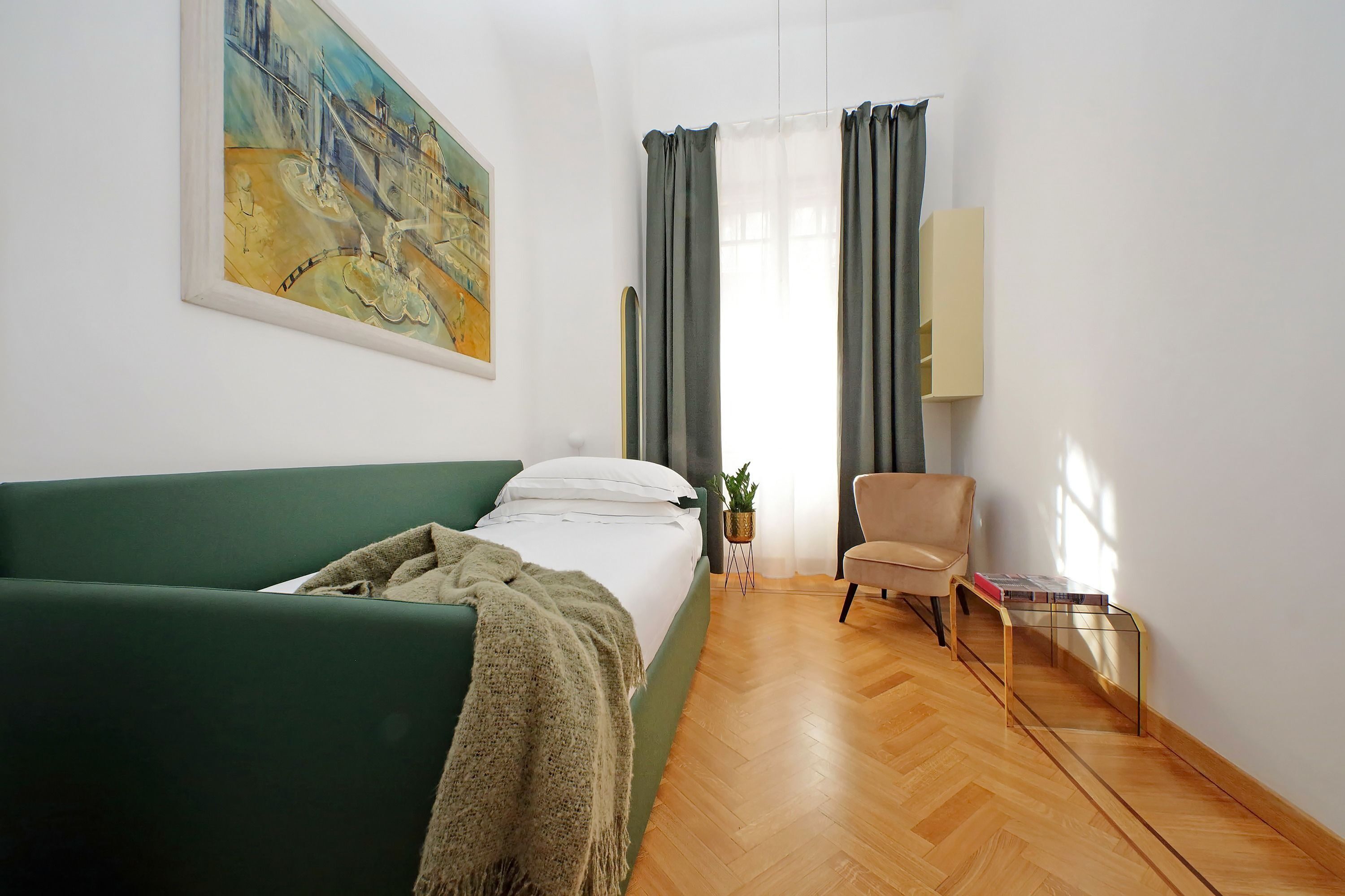 Ein Zimmer mit einem Bett, einem grünen Sofa, einem Sessel, einem kleinen Tisch, einer Pflanze und einem Gemälde an der Wand.
