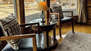 Een gezellige kamer met een groot raam, een ronde tafel, twee stoelen en een lamp.
