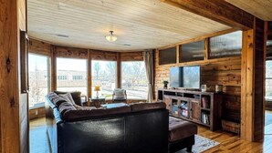 Een gezellig houten blokhutinterieur met een groot houten plafond, een zwarte leren bank, een televisie en een houten kast.