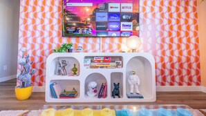 A living room with a TV mounted on a wall displaying various streaming services. - Near Airport: Game Room, Mini Golf, Cowboy Pool, Smart TVs & Air Purifiers (Commerce City)