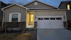 A residential house with a garage, a front door with a light, and a small front yard. - Near Airport: Game Room, Mini Golf, Cowboy Pool, Smart TVs & Air Purifiers (Commerce City)