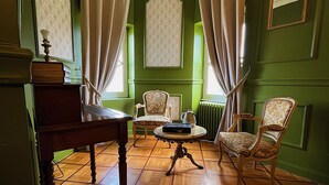Una stanza con pareti verdi, pavimento in legno, un tavolo con un libro e un bollitore, due sedie e un termosifone.