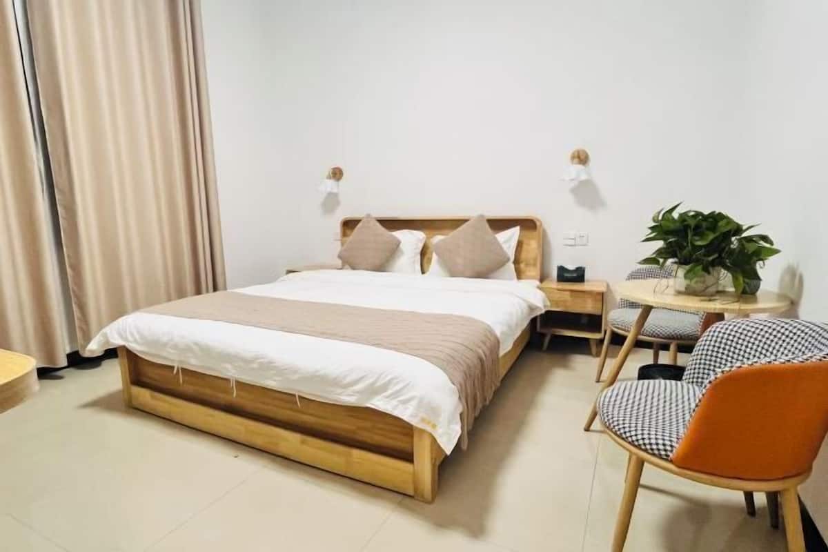 A bedroom with a wooden bed, bedside tables, a small round table with a plant, and a chair.